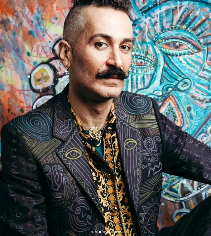 Marco Scola in one of his own hand-painted jackets, in front of one of his paintings.