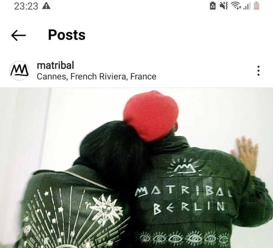 Two people from behind wearing green jackets hand-painted with MATRIBAL BERLIN and an eye motif.
